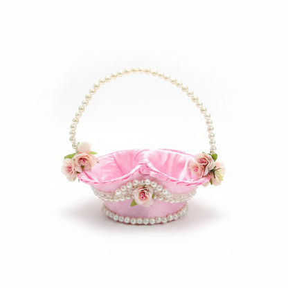 A decorative pink satin handbag with a pearl-bead handle and trim, adorned with small white and pink flowers, resting on a brown quilted chair.