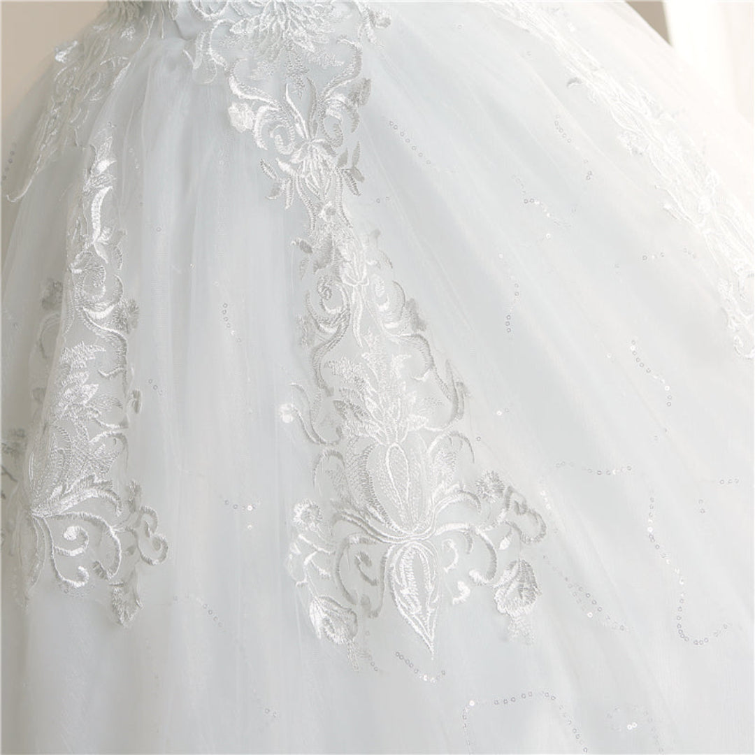 White bridal gown with lace appliqué details, elegant neckline, and flowing cathedral train by GownLink